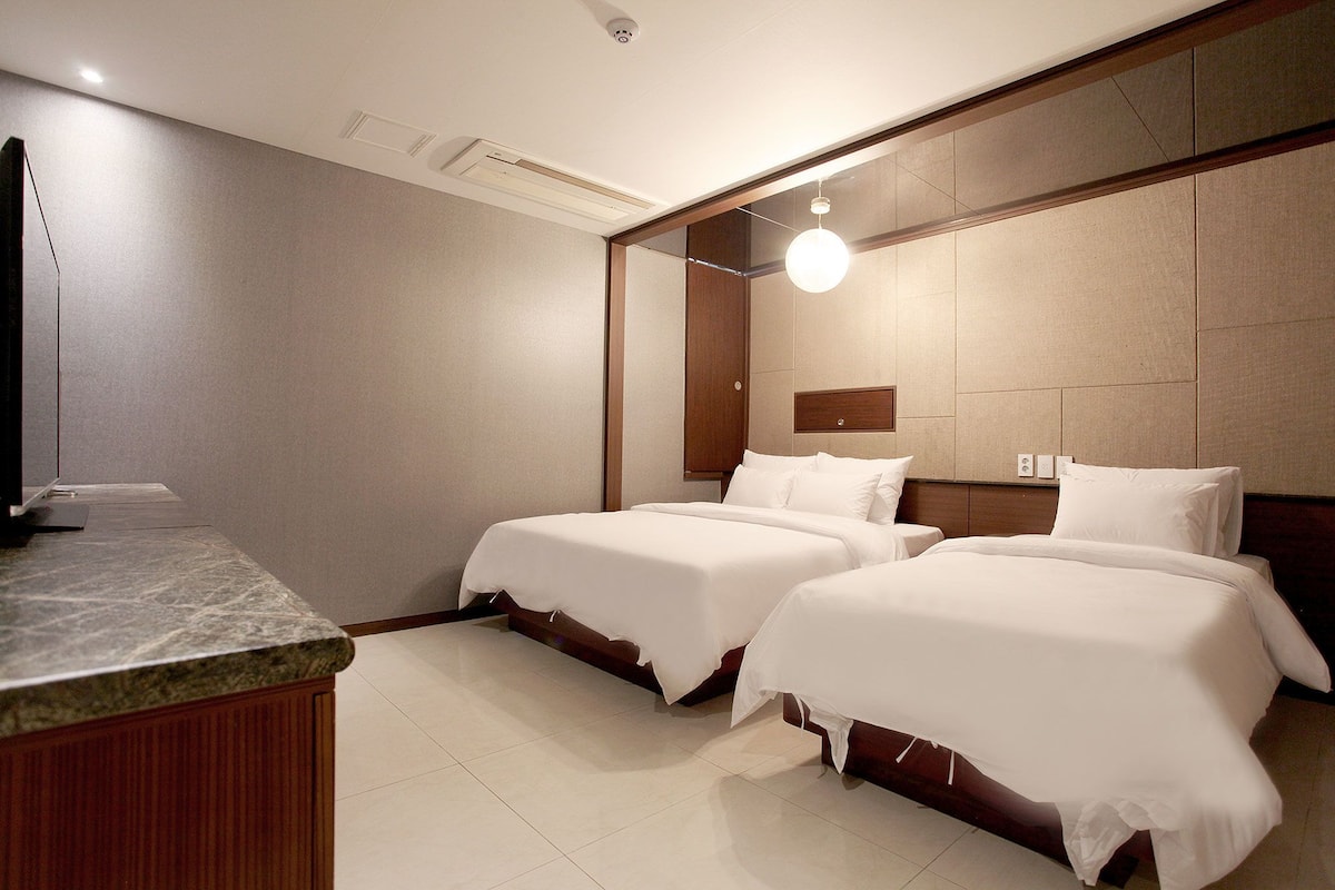 A hotel room with two beds, a wooden headboard, a marble counter, and a ceiling-mounted light fixture.