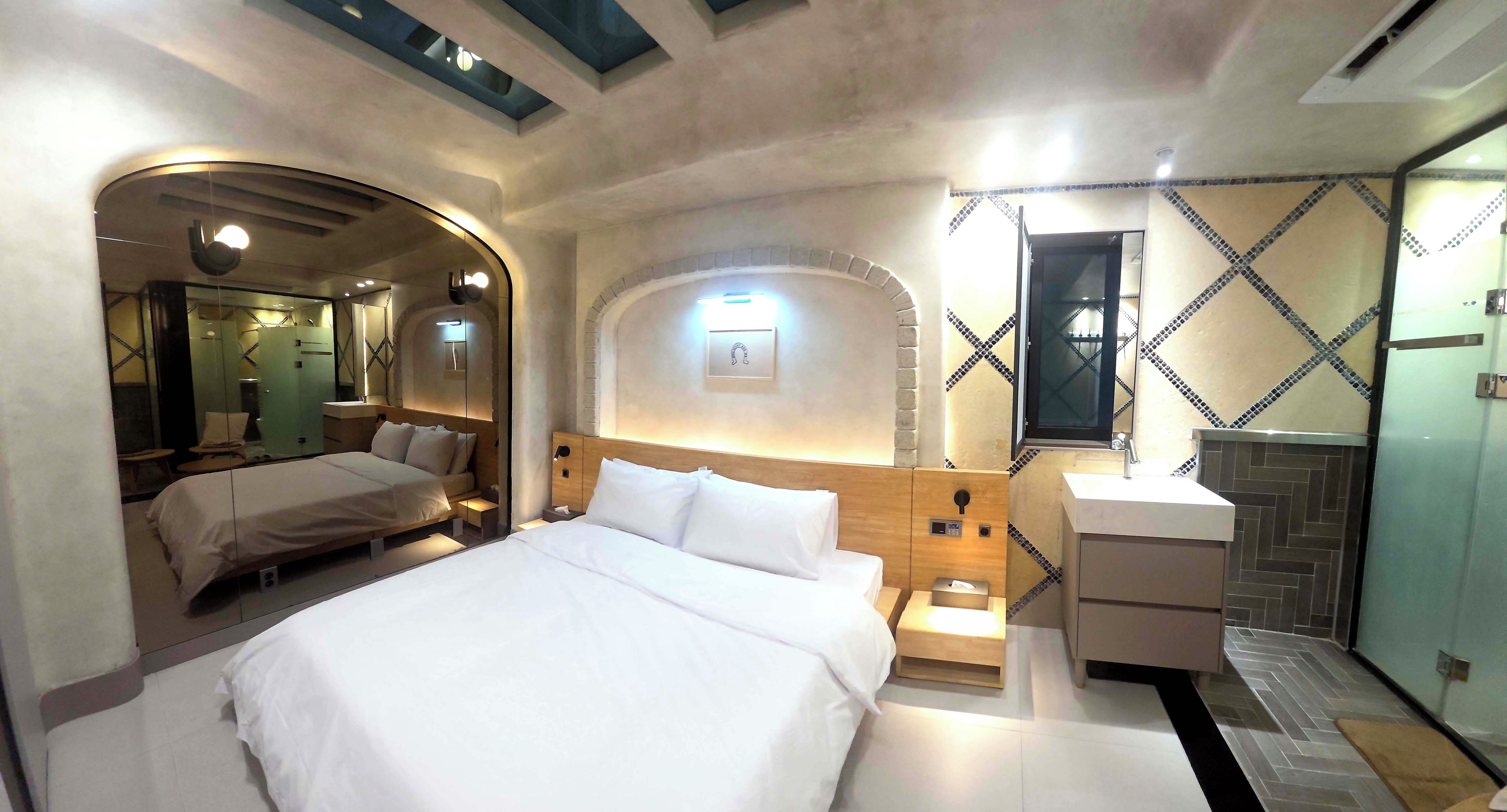 Une chambre d’hôtel avec un grand lit, des tables de chevet, un miroir et un espace douche.