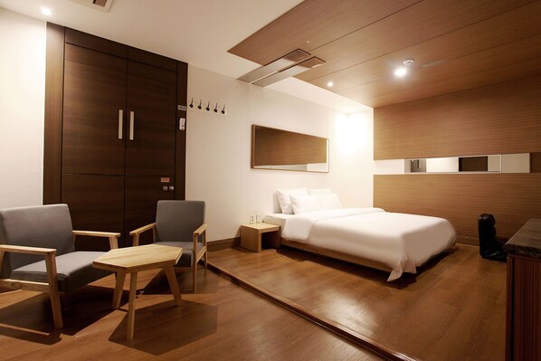 A modern hotel room with a bed, two chairs, a small table, a wooden wardrobe, a nightstand, and a mirror. - The Ace Hotel (Seoul)
