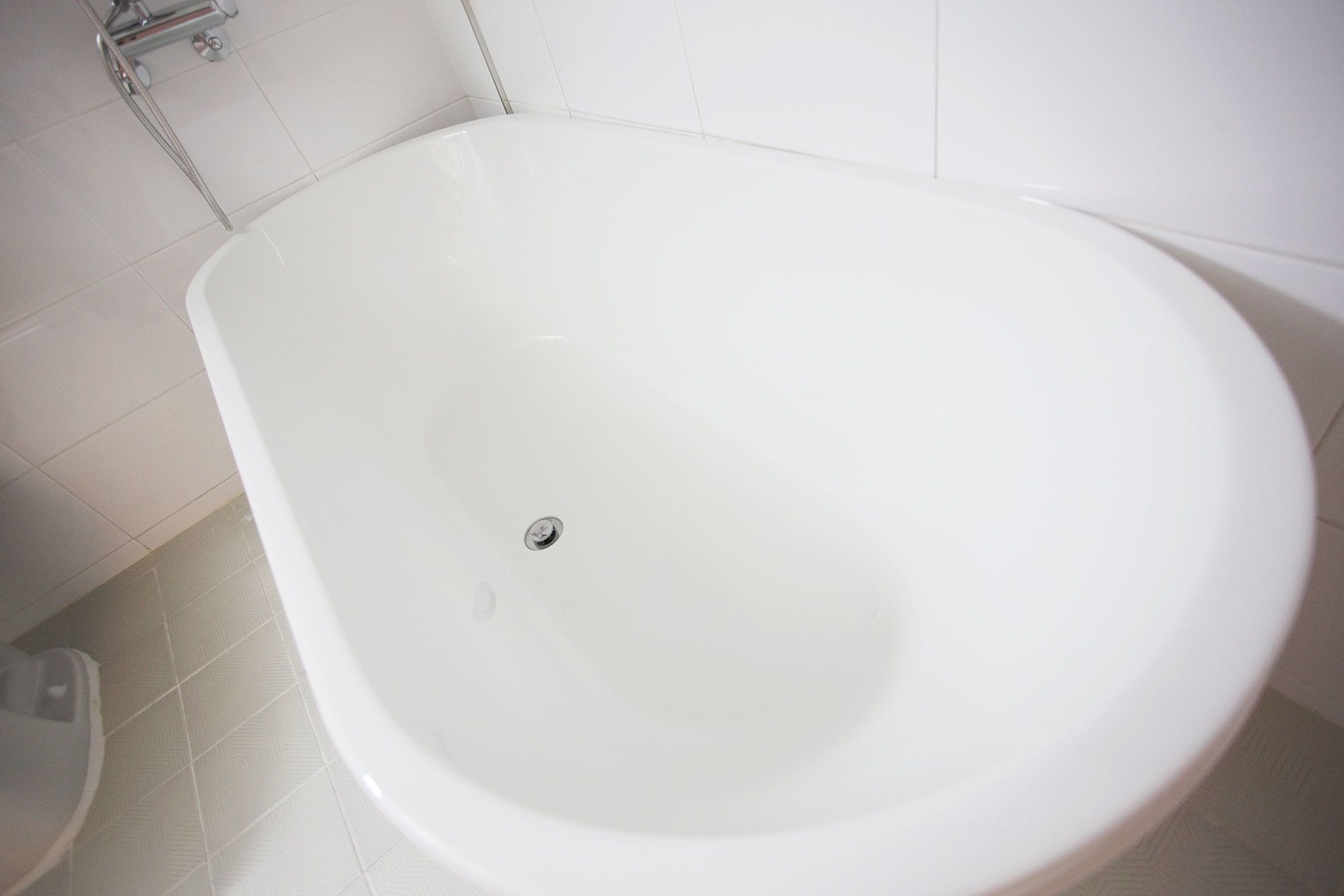 Une baignoire blanche, sur pieds, dans une salle de bain aux carreaux blancs.