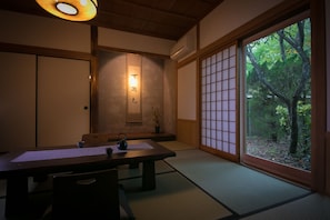 Une pièce de style japonais traditionnel, avec un sol recouvert de tatamis, une petite table et une théière, ainsi qu’une porte coulissante donnant sur un jardin.