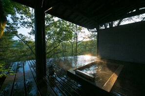 A wooden deck with a hot tub and a view of a forest. - Shukubo Kawaseminoshou - The Kingfisher resort - (Taketa)