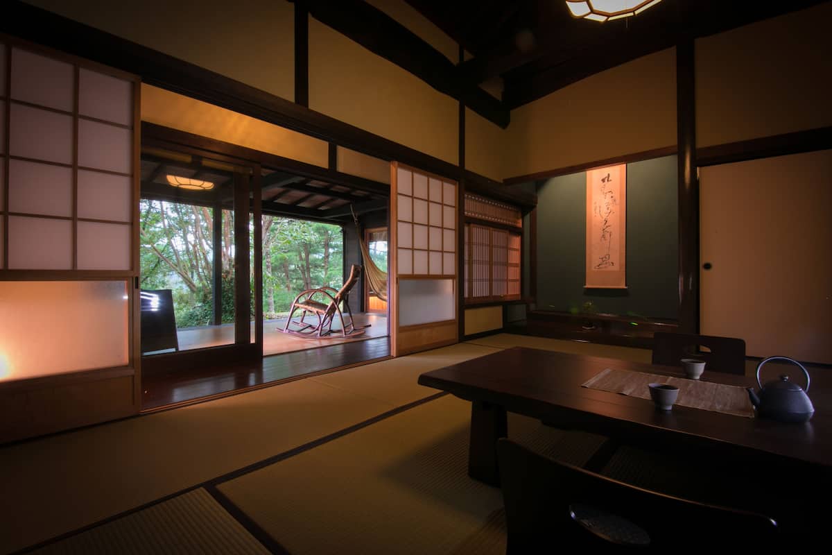 Ein traditioneller japanischer Raum mit Tatami-Böden, Schiebetüren und einem niedrigen Tisch mit Teekanne und Tassen.