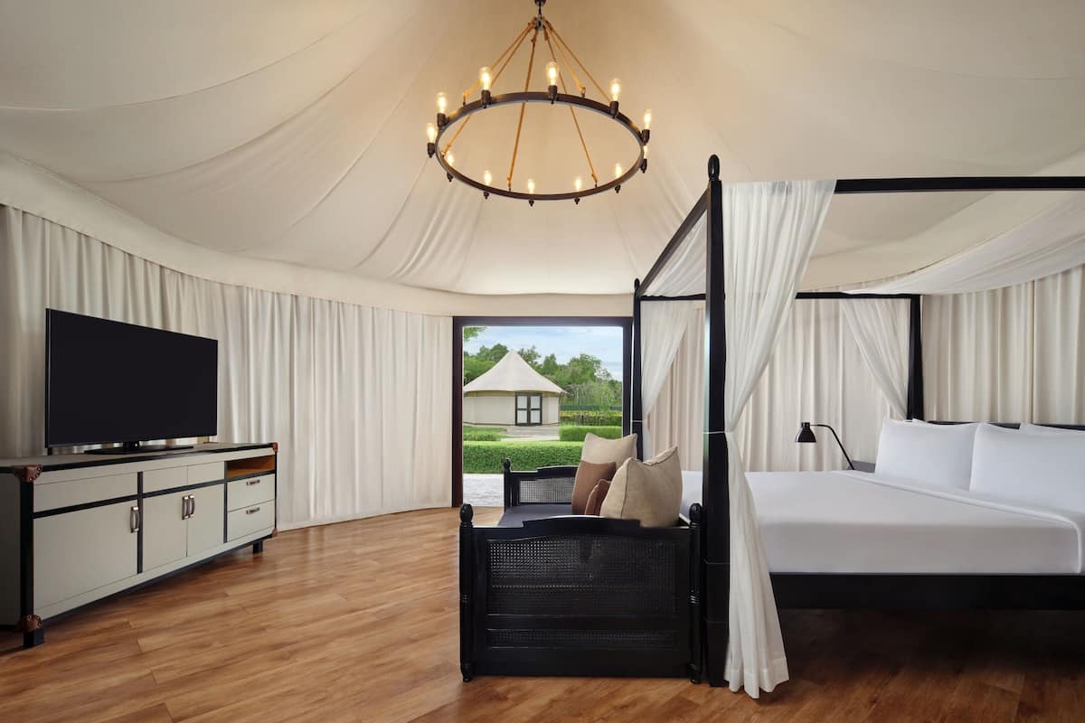 Une chambre spacieuse avec un grand lit, un téléviseur posé sur un meuble et une vue sur une maison par la fenêtre.
