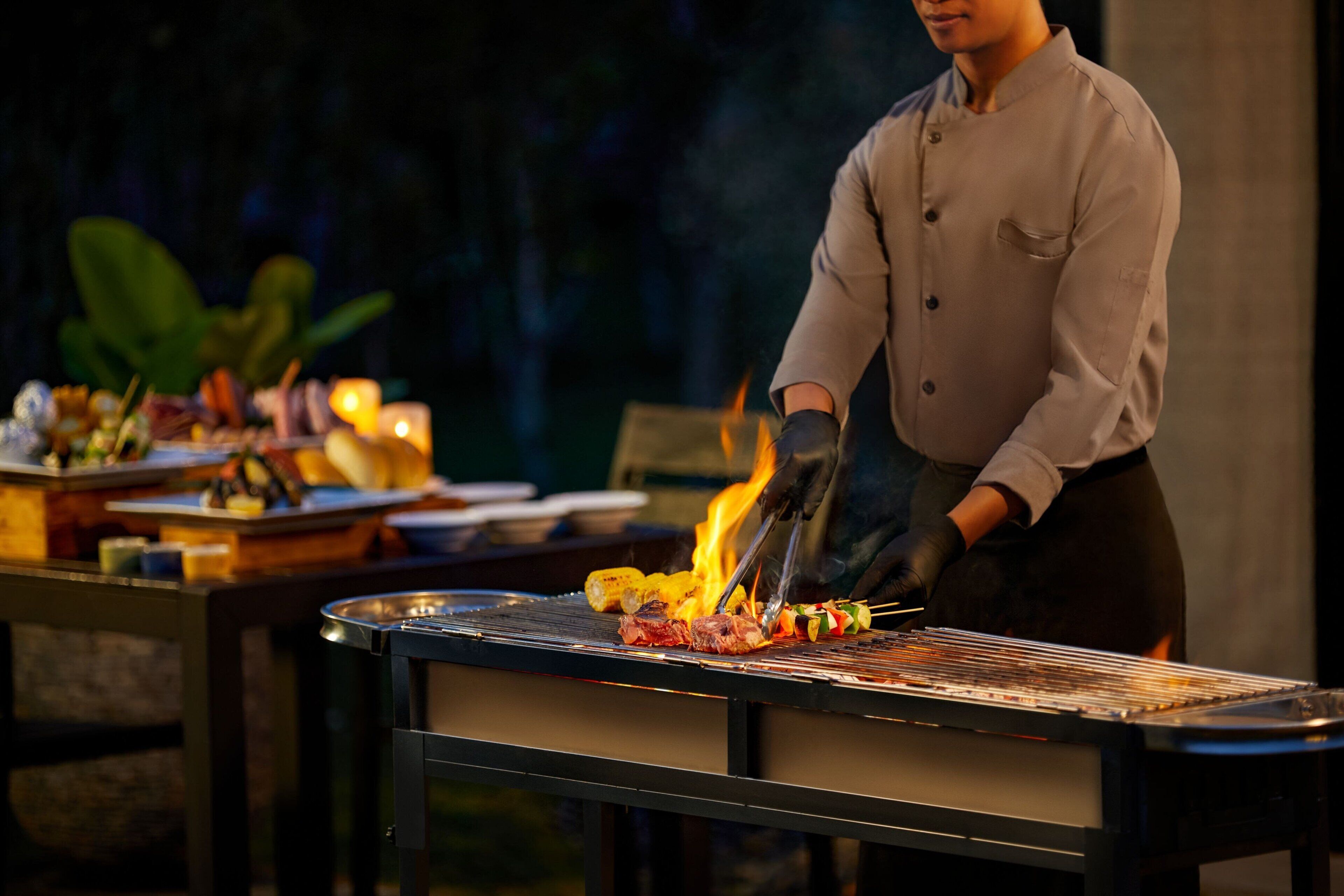 A chef grilling meat and vegetables on an outdoor grill.