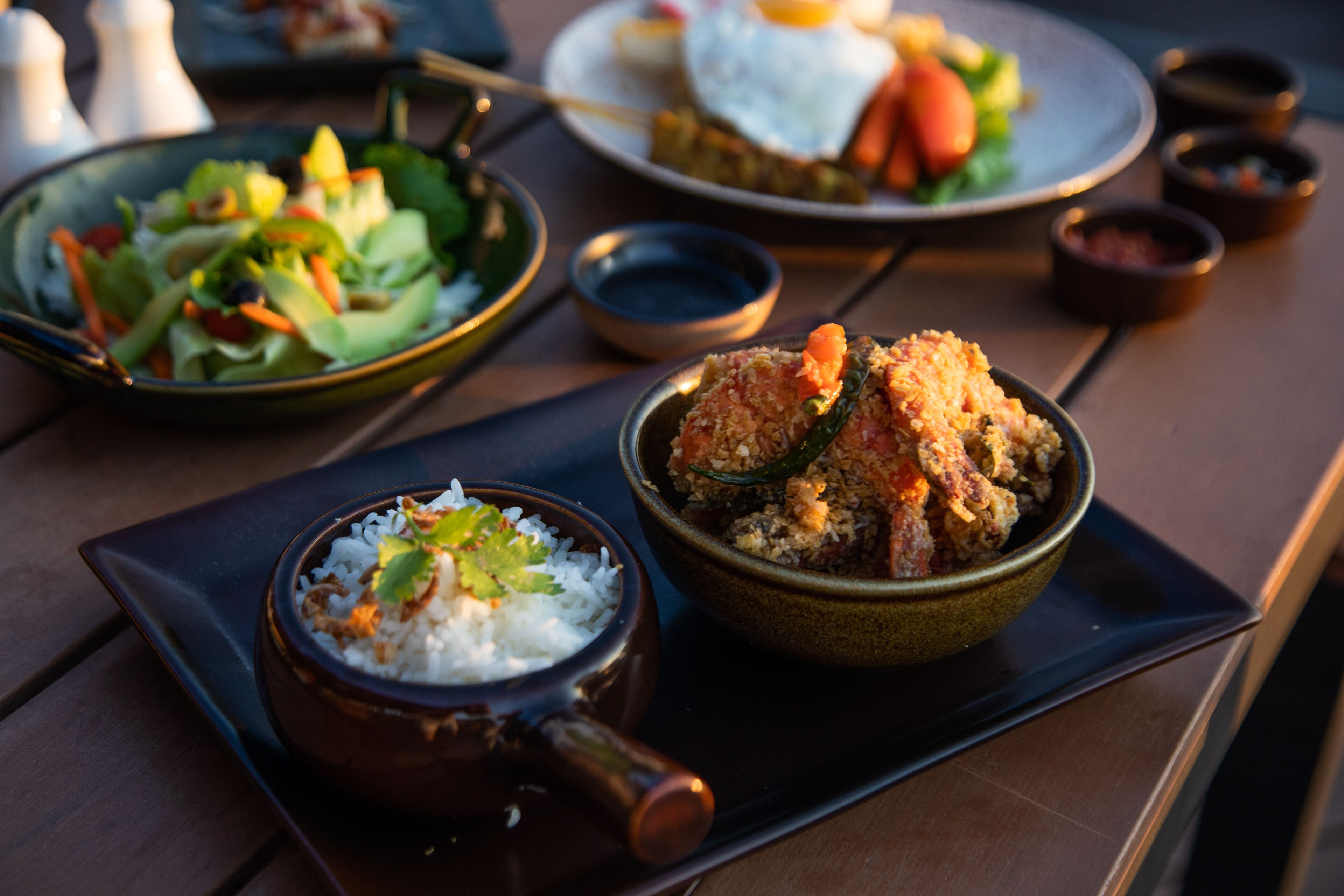 A table with various dishes including rice, a salad, and a bowl of fried food.