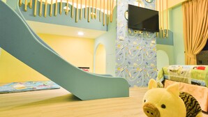 A children's play area with a slide, a TV mounted on a wall, and a plush toy on the floor. - Minsuku (Taitung)