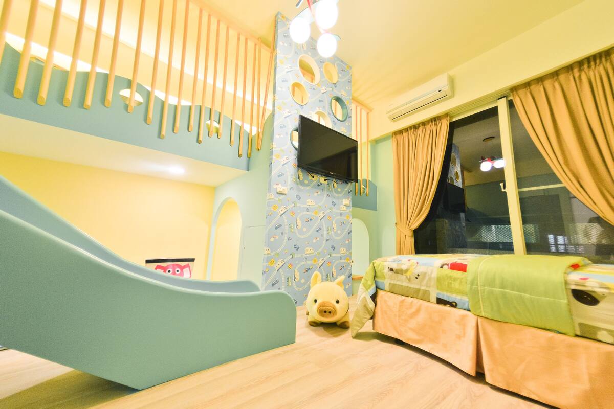 A children's playroom with a slide, a bed, and a TV mounted on the wall.