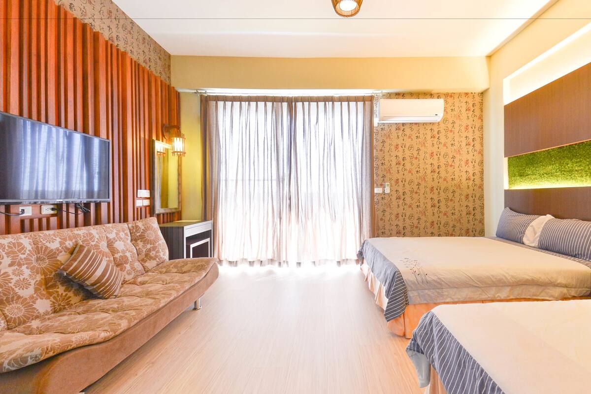 A hotel room with a sofa, a bed, a TV, and a window with curtains.