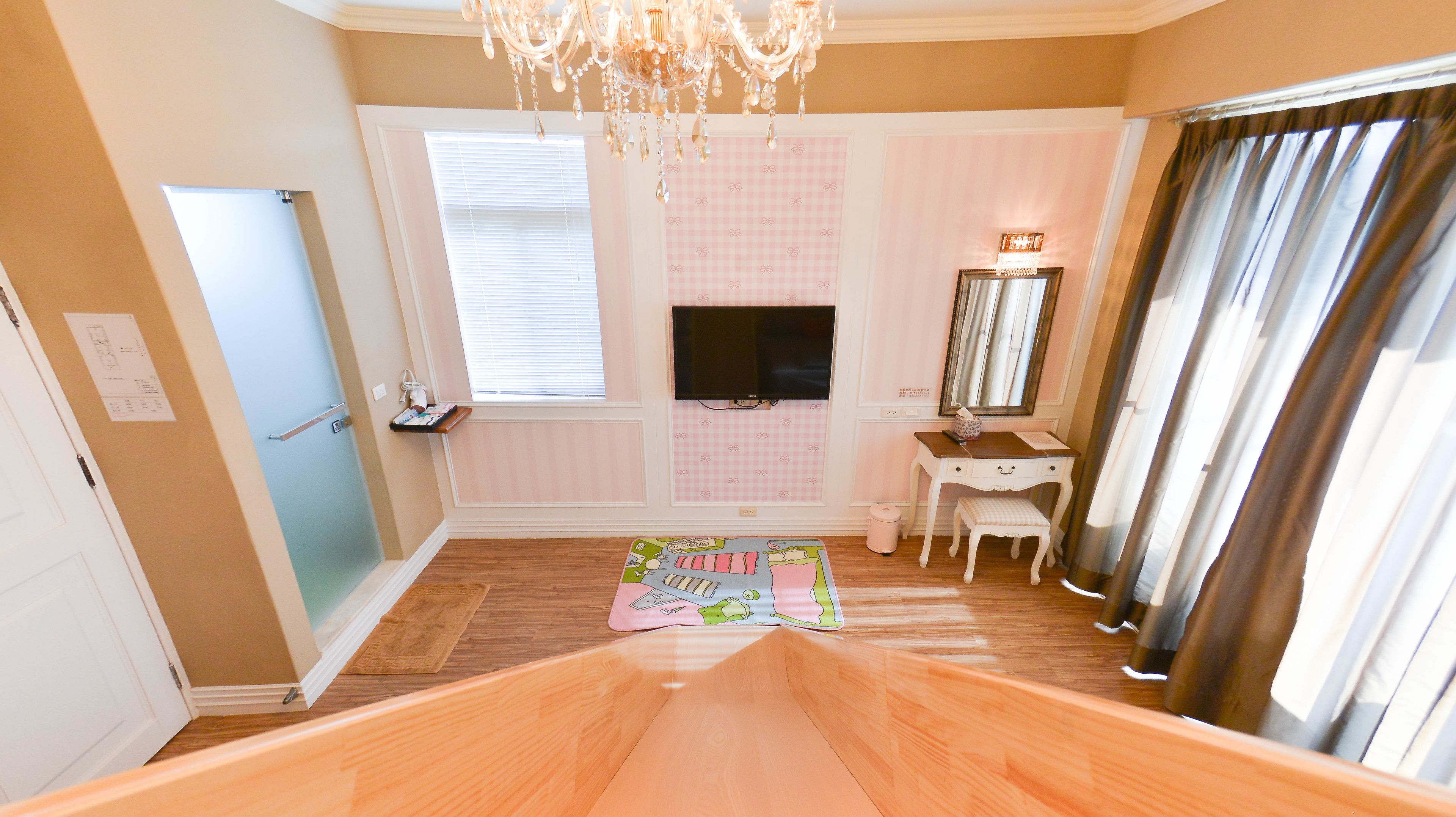 A bedroom with a wooden floor, a vanity with a mirror, a television on the wall, and a window with blinds.