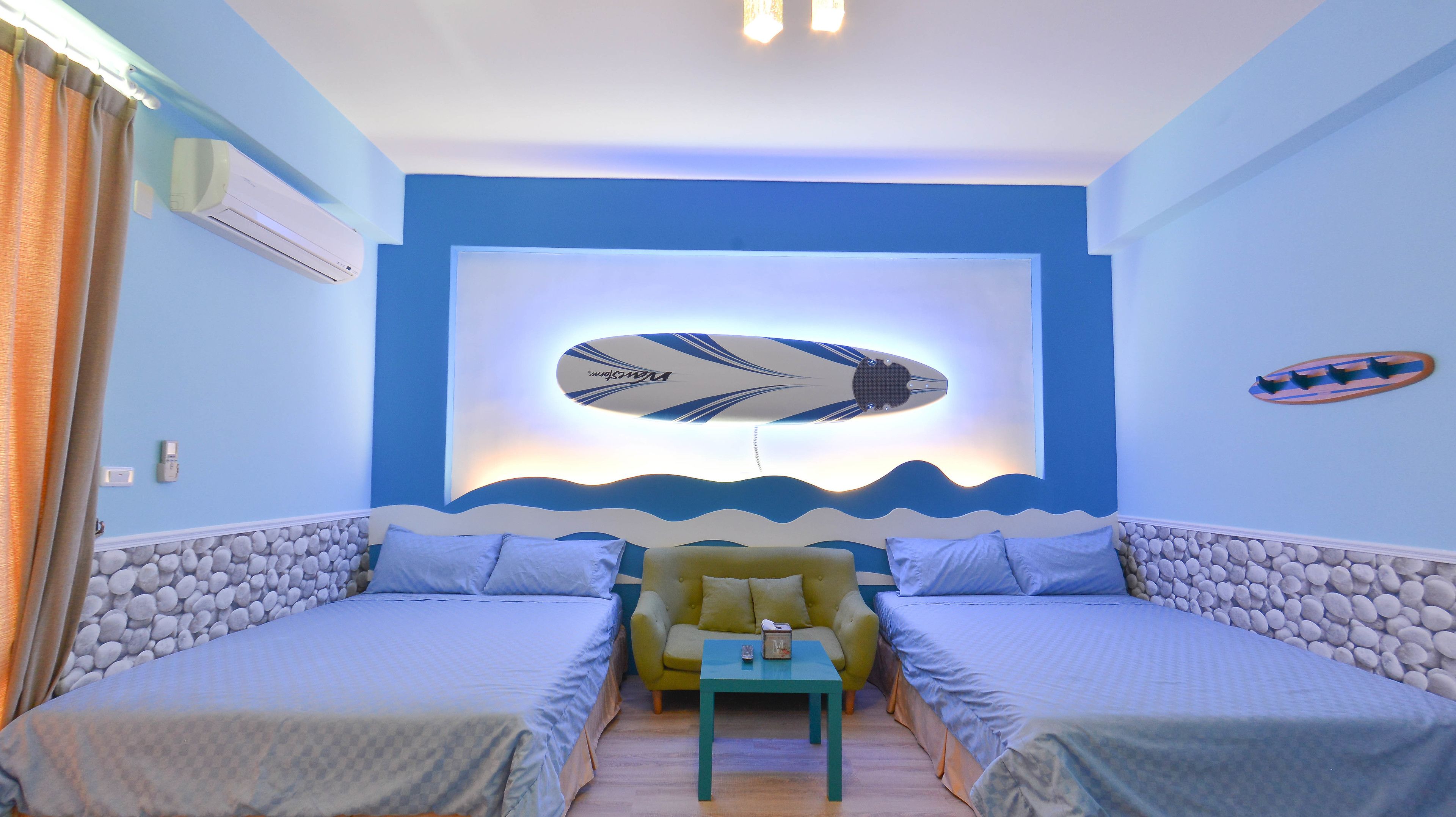 A room with two beds, a small table, and a wall-mounted surfboard decoration.