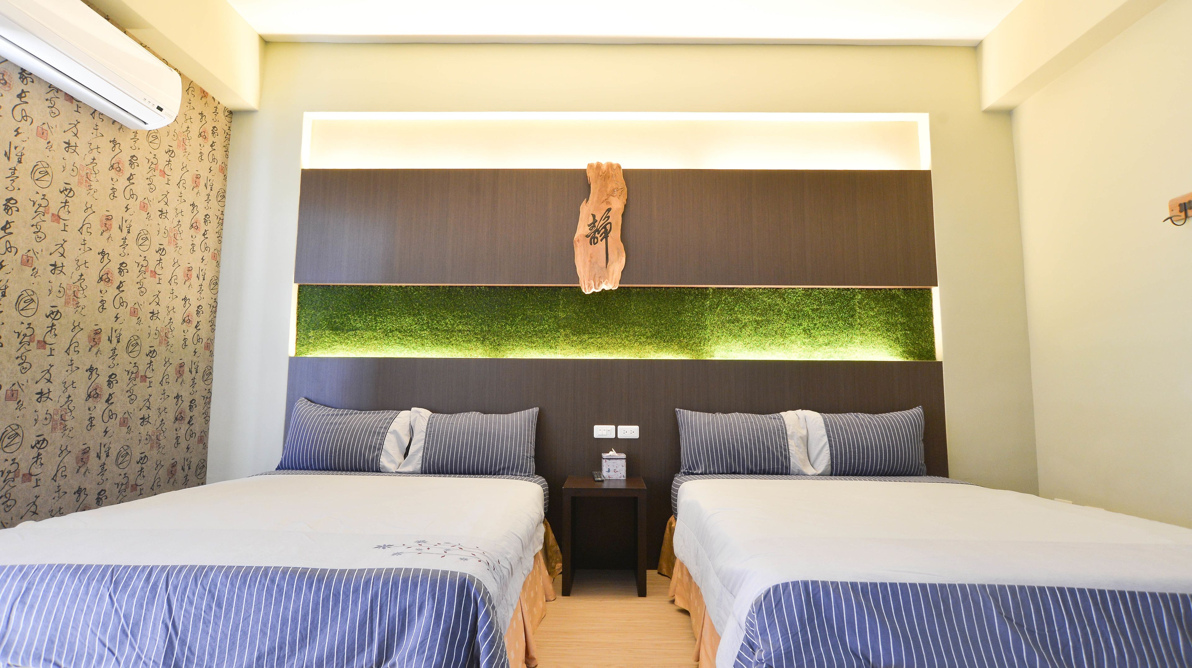 A hotel room with two beds, a nightstand, and a wall-mounted air conditioner.