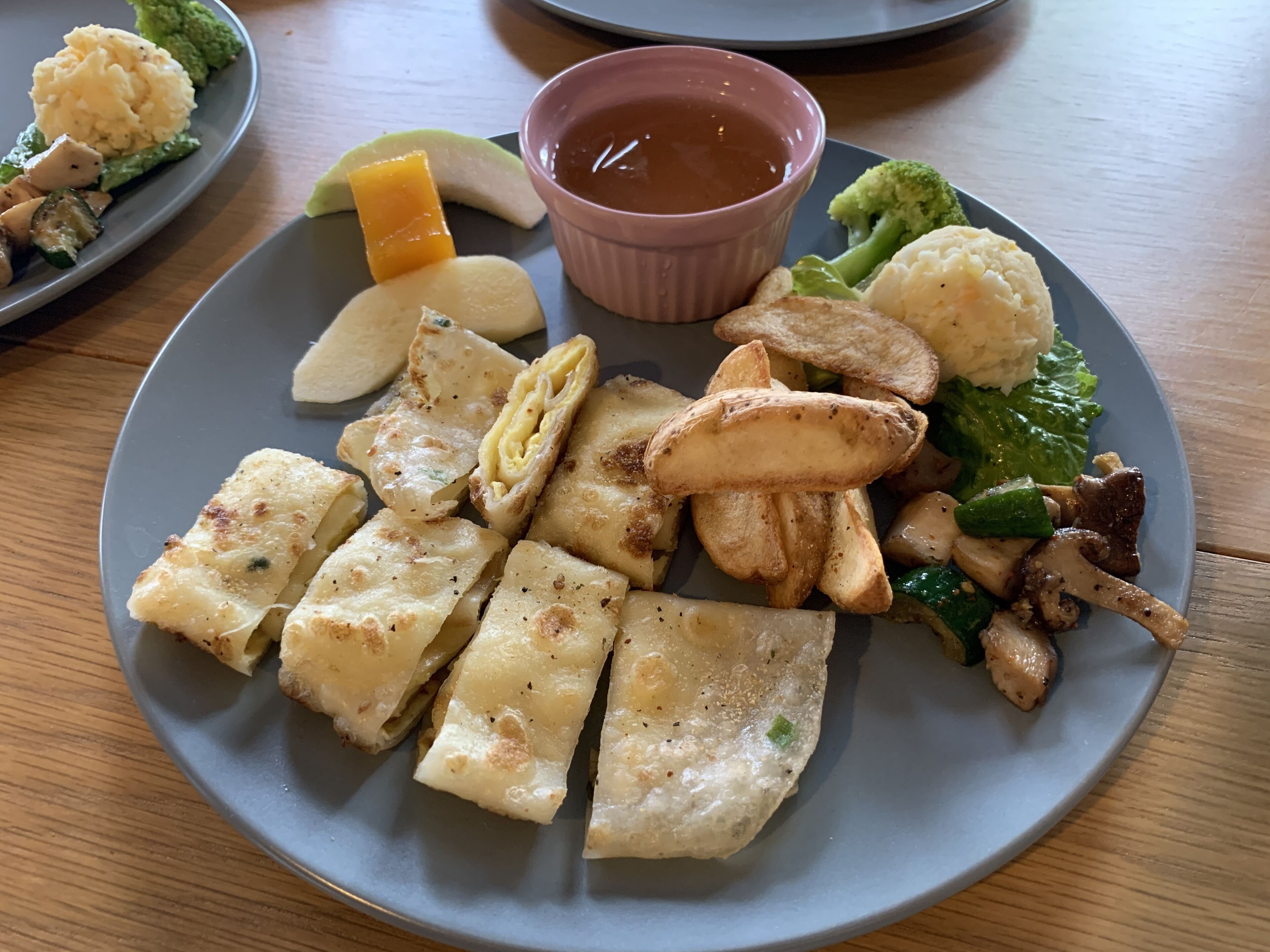 A plate with various food items including tofu, potatoes, and vegetables, accompanied by a small bowl of sauce.