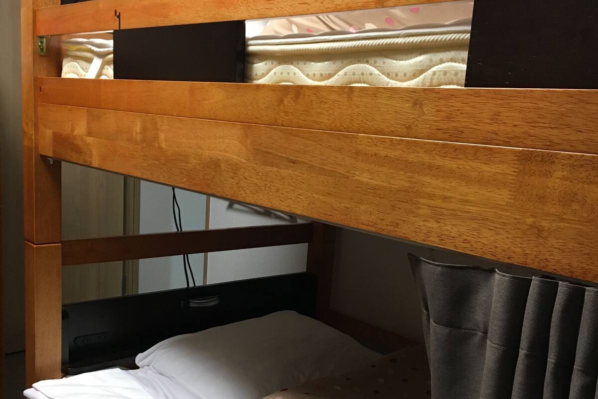 Ein Etagenbett mit Holzbettrahmen, eine Matratze mit Punkten und ein weißes Kopfkissen.