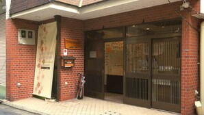 Un bâtiment en briques avec une enseigne indiquant « Guest House Kyoto Inn » et un portail métallique fermé.