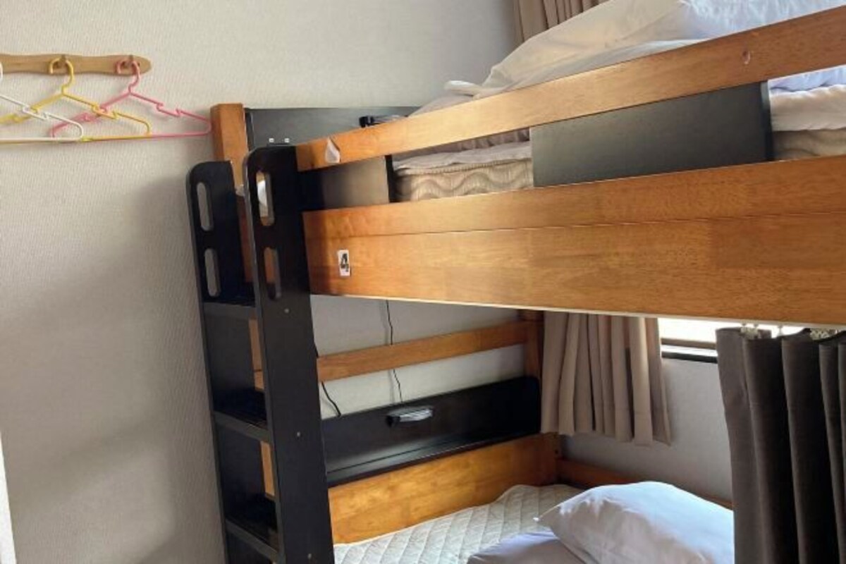 A bunk bed with a wooden frame, a small shelf, and a curtain.