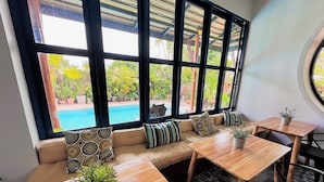 A cozy seating area with a pool view, wooden tables, and potted plants. - The Luna Hostel (Sa Khu)