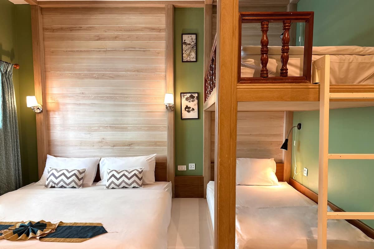 Una habitación de hotel con cabecera de madera, literas y una cama con ropa blanca y almohadas estampadas.