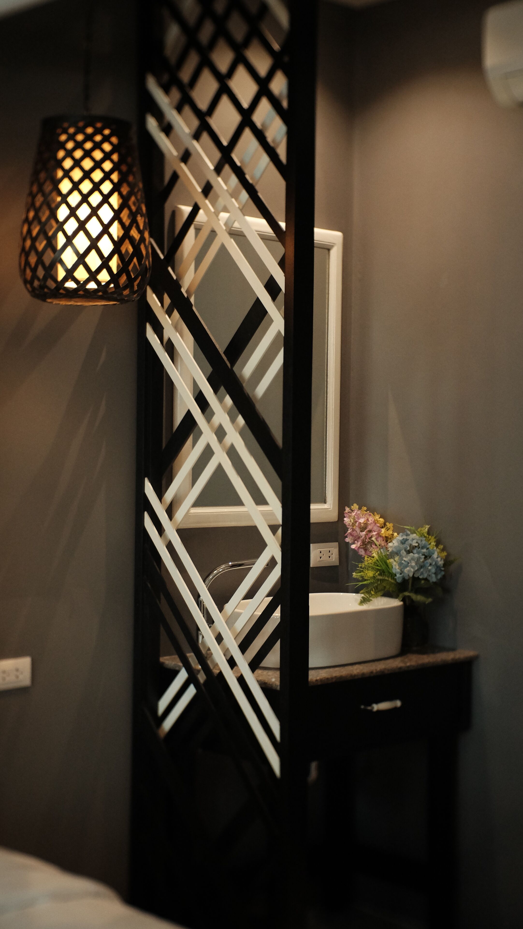 Un baño moderno con un separador geométrico blanco y negro, un lavamanos blanco y un jarrón decorativo con flores.
