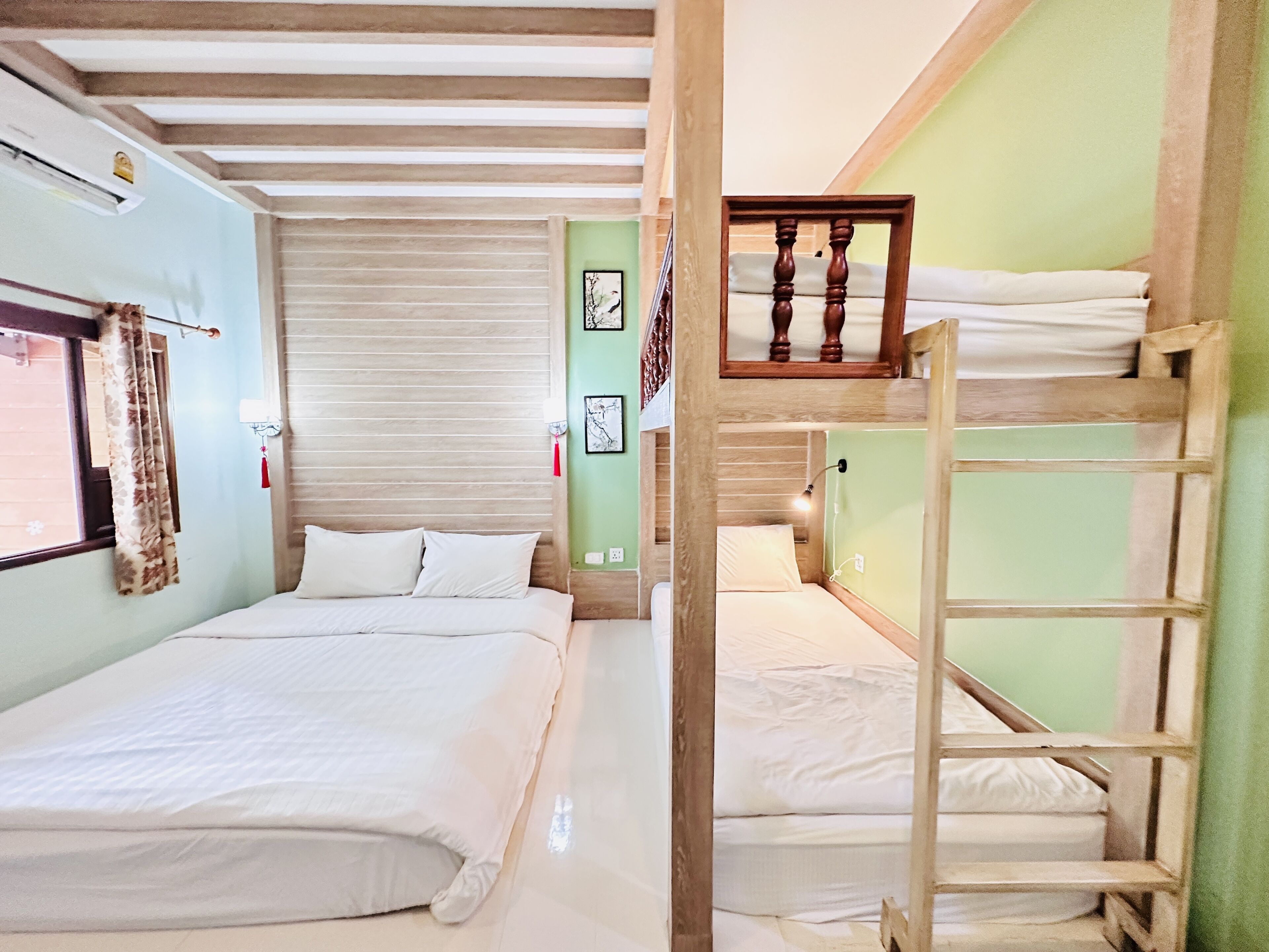 Una habitación con dos camas, una escalera de madera, una ventana con cortinas y un aire acondicionado de pared.