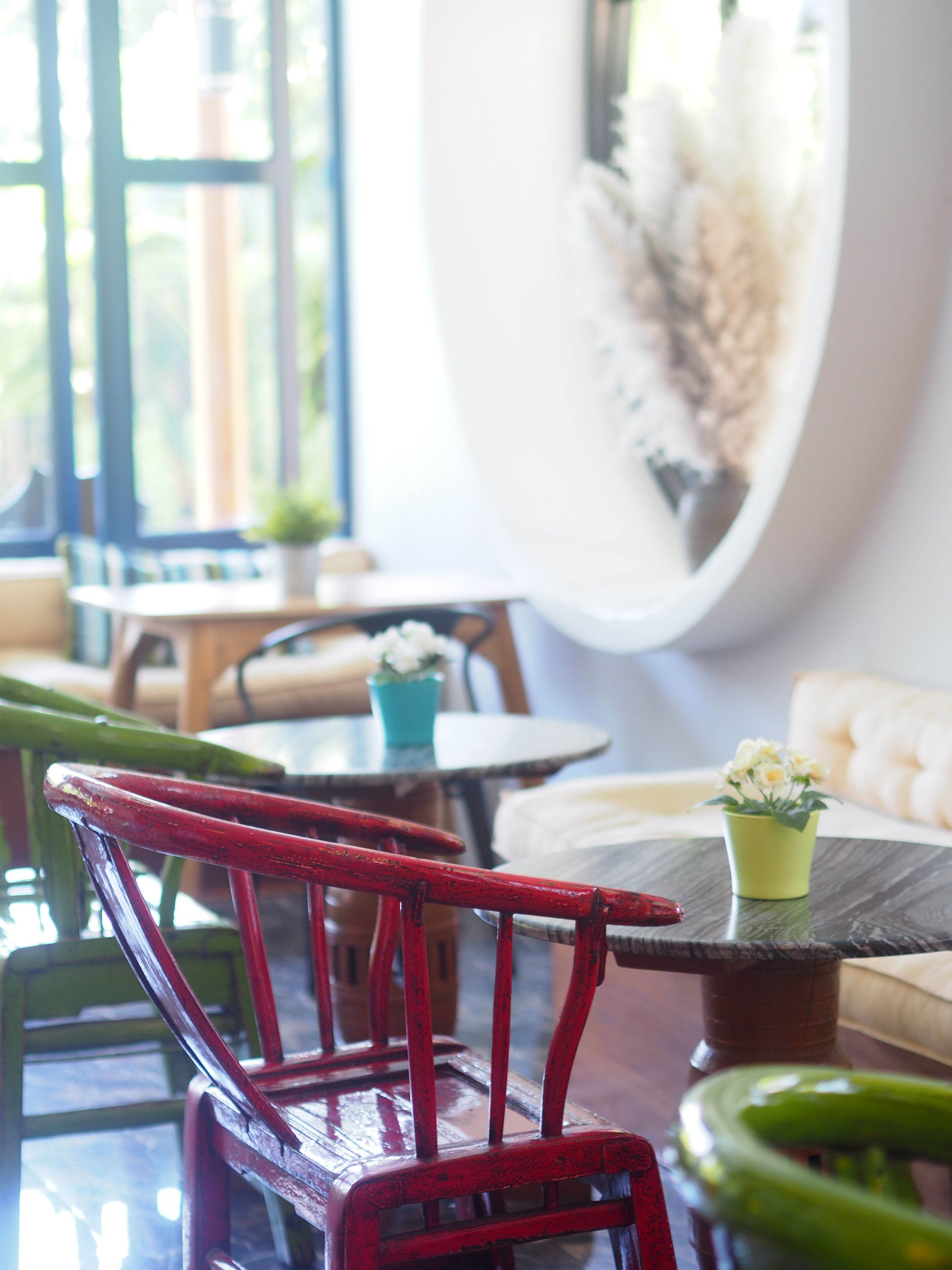 Un espace de détente intérieur accueillant, avec un fauteuil rouge, une table ronde ornée d’un pot vert et un canapé blanc.