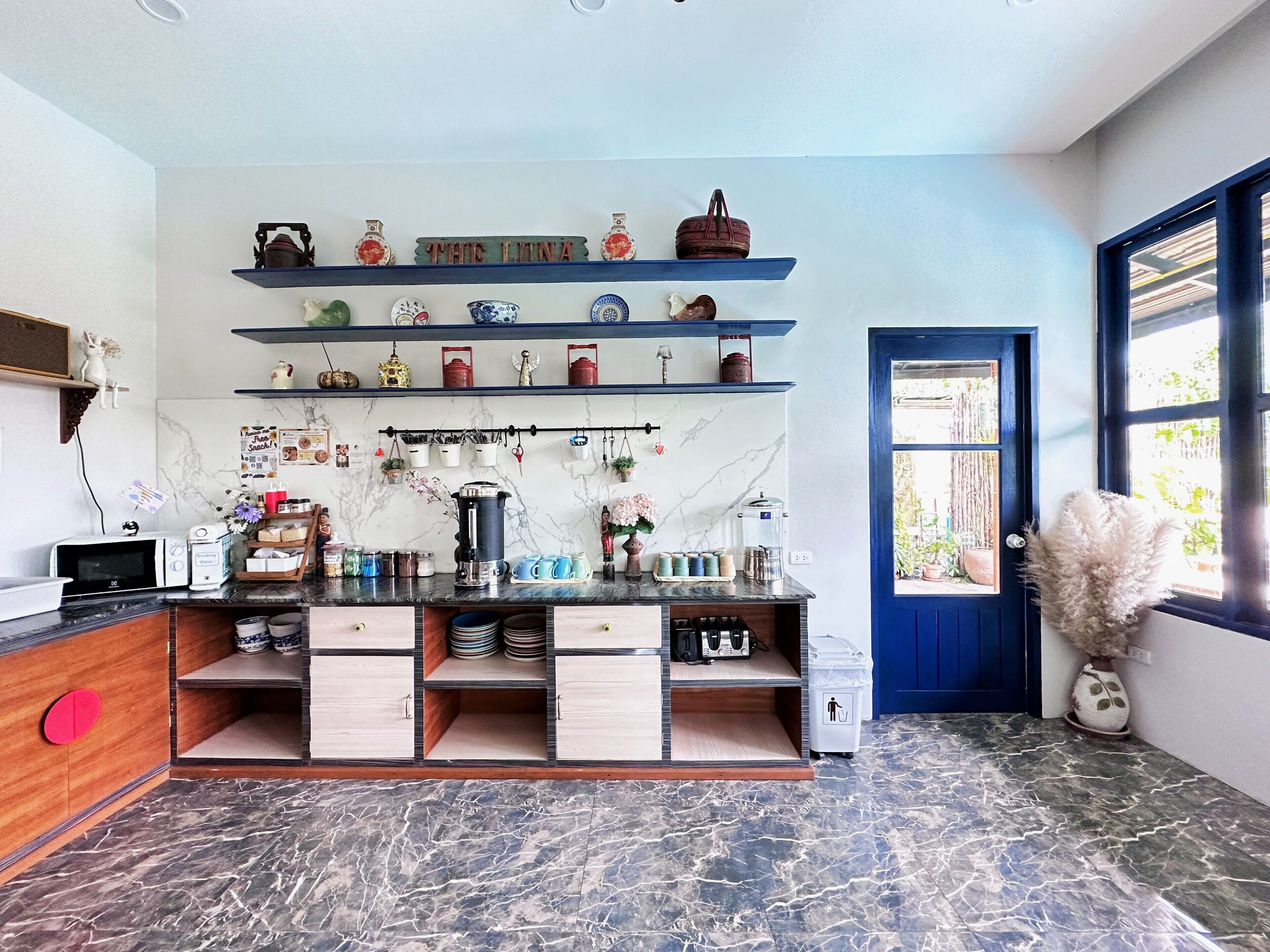 A kitchen with marble countertops, a coffee machine, and shelves with decorative items.