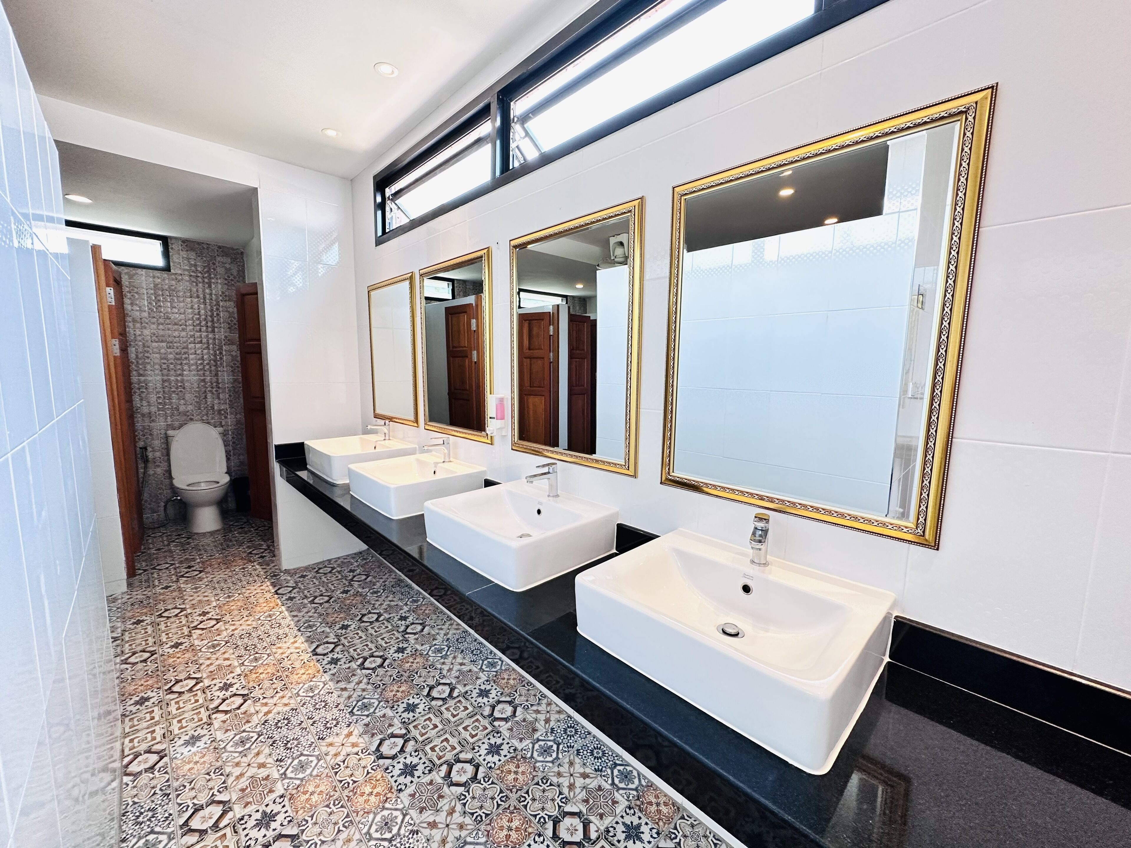 Un bagno moderno con tre lavabi, ampi specchi e piastrelle a motivi decorativi.