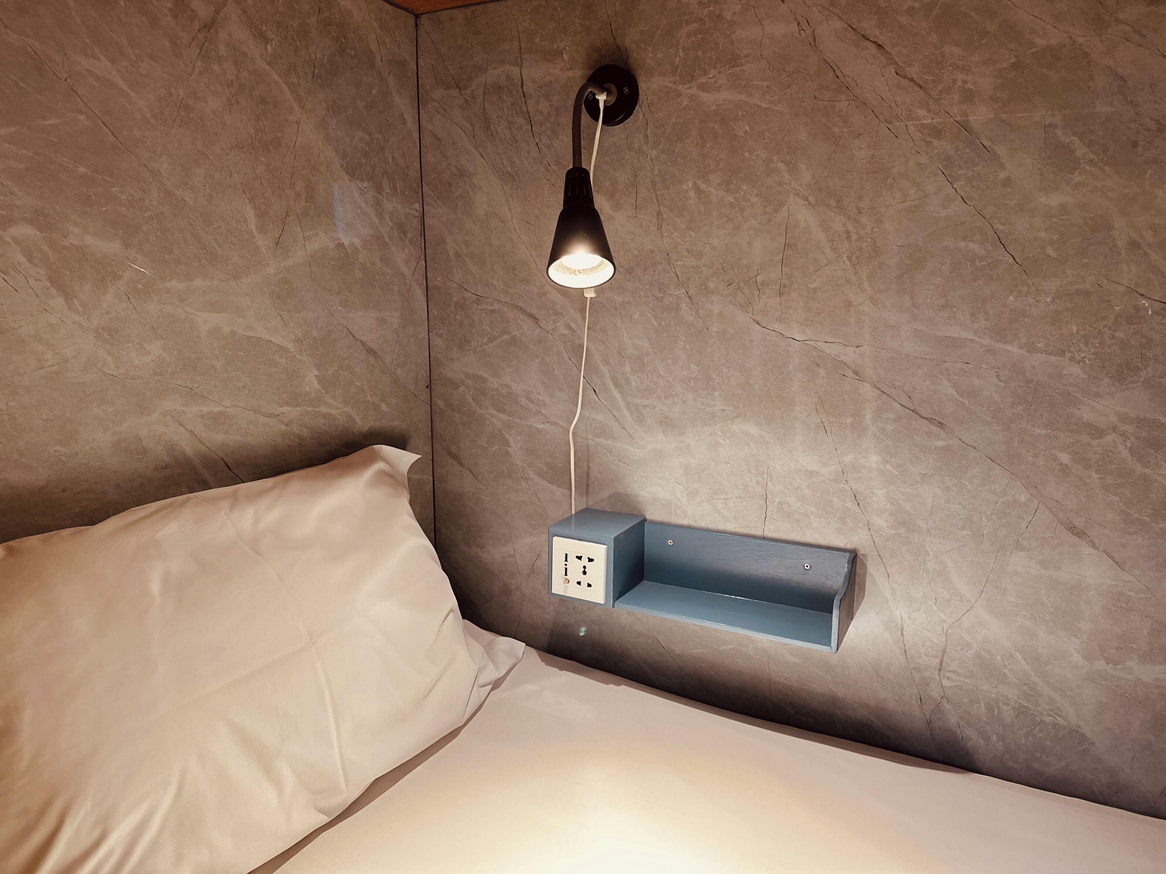 Un dormitorio con una cama, una mesita de noche fijada a la pared y una lámpara de pared.