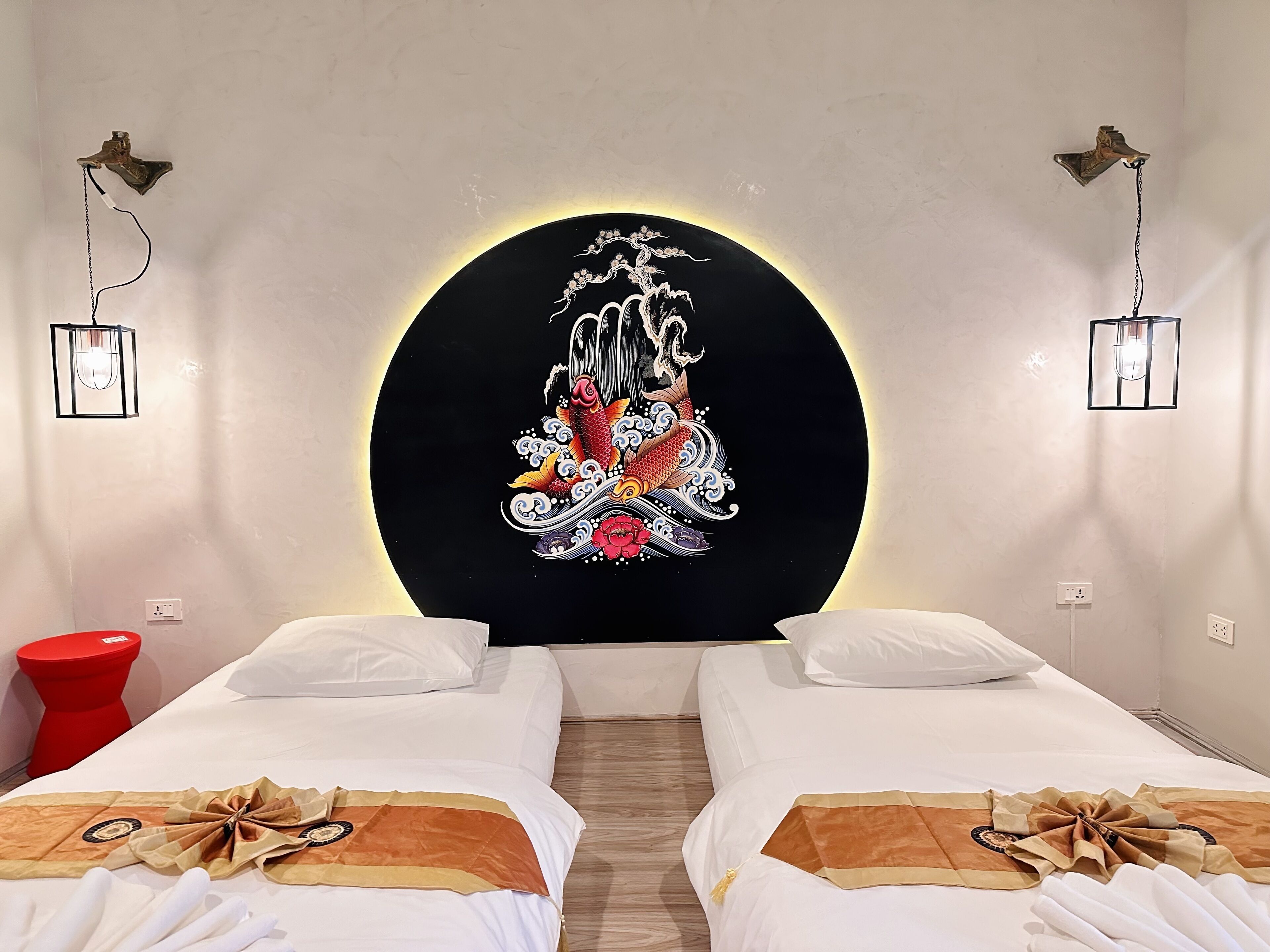 Habitación de hotel con dos camas, un taburete rojo y una obra de arte circular grande en la pared.