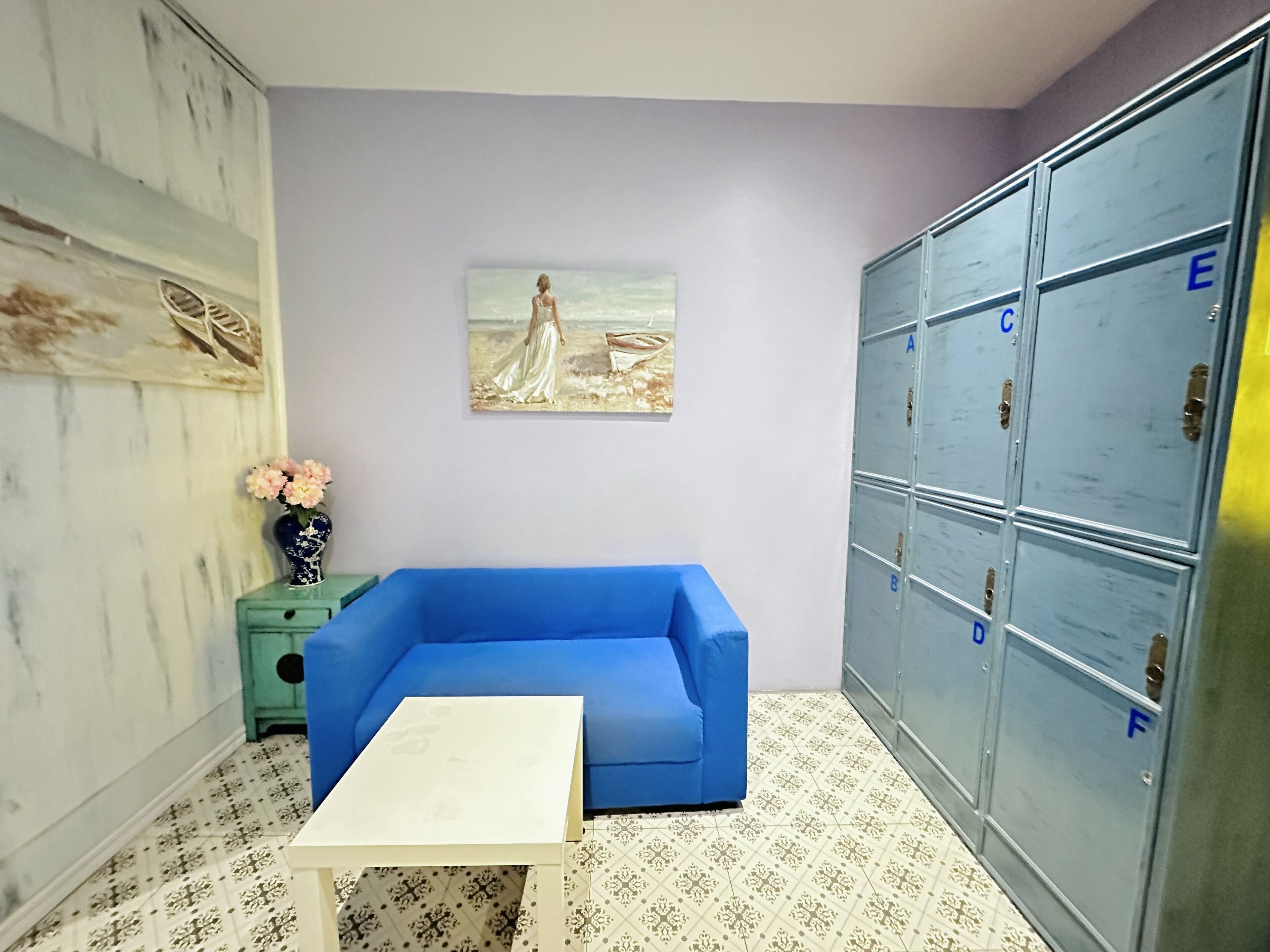 A room with a blue sofa, a white table, a painting, and metal lockers.