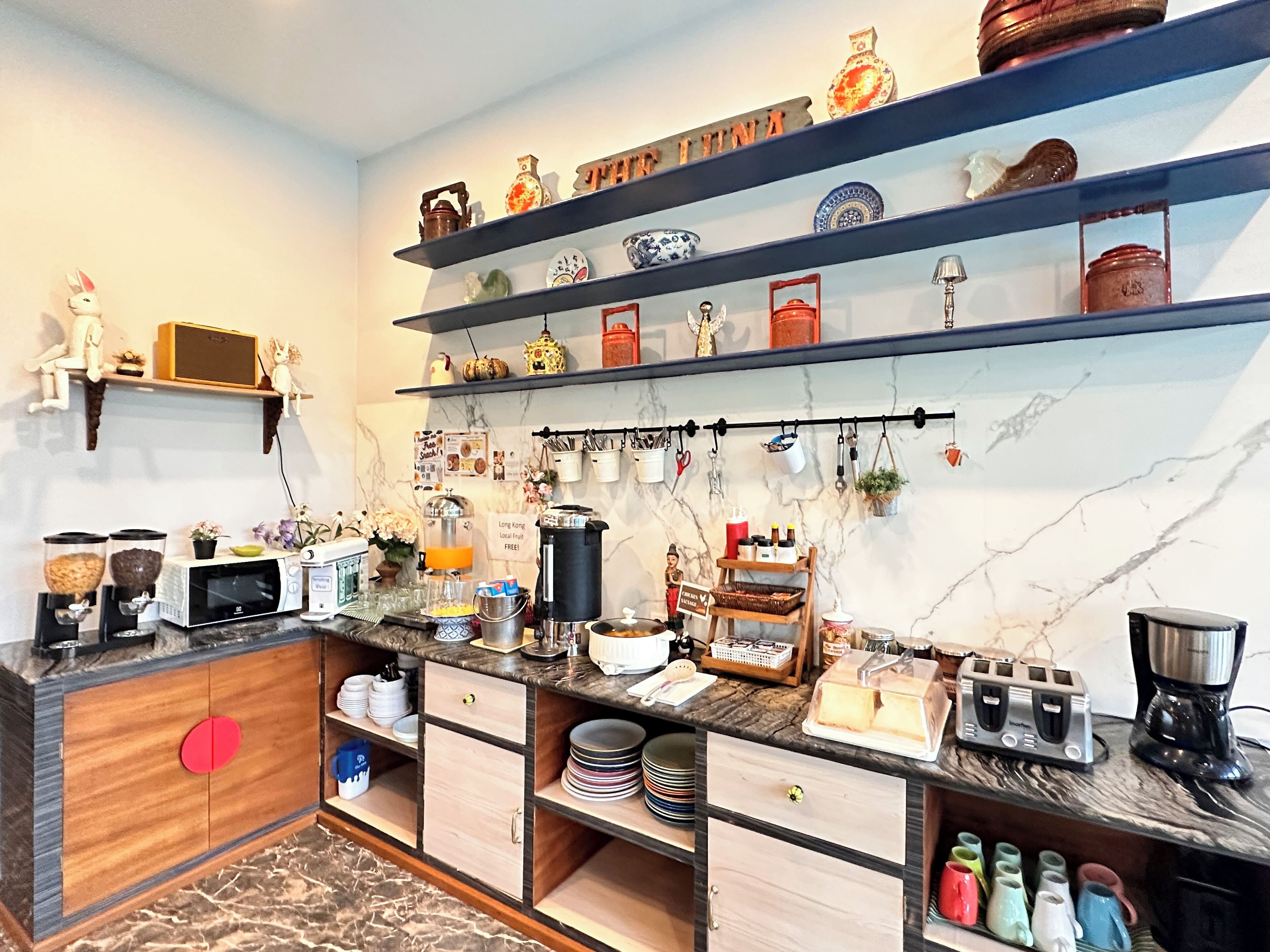 A kitchen with a marble countertop, a microwave, a coffee maker, and shelves with decorative items.