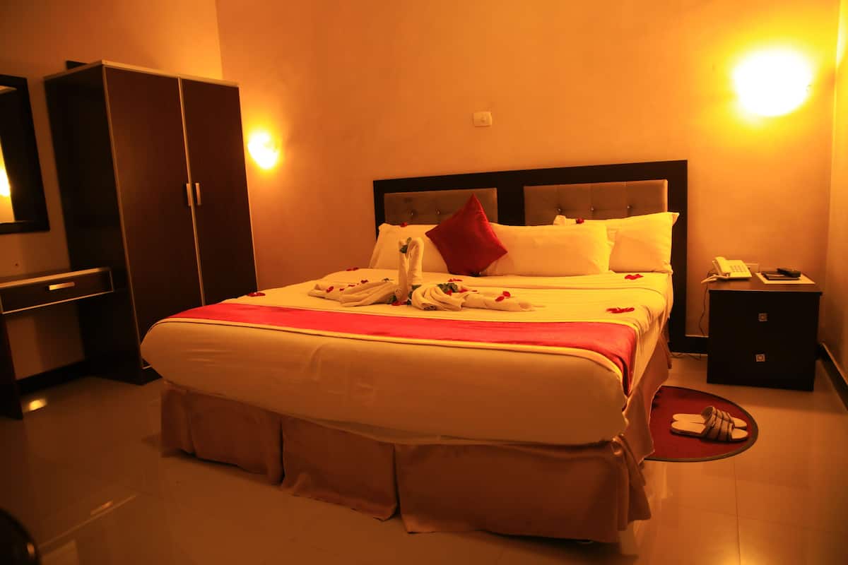 A hotel room with a large bed, a wardrobe, a bedside table with a phone, and a red rug.