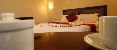 A hotel room with a bed, pillows, a bedside table, and a wall-mounted light.