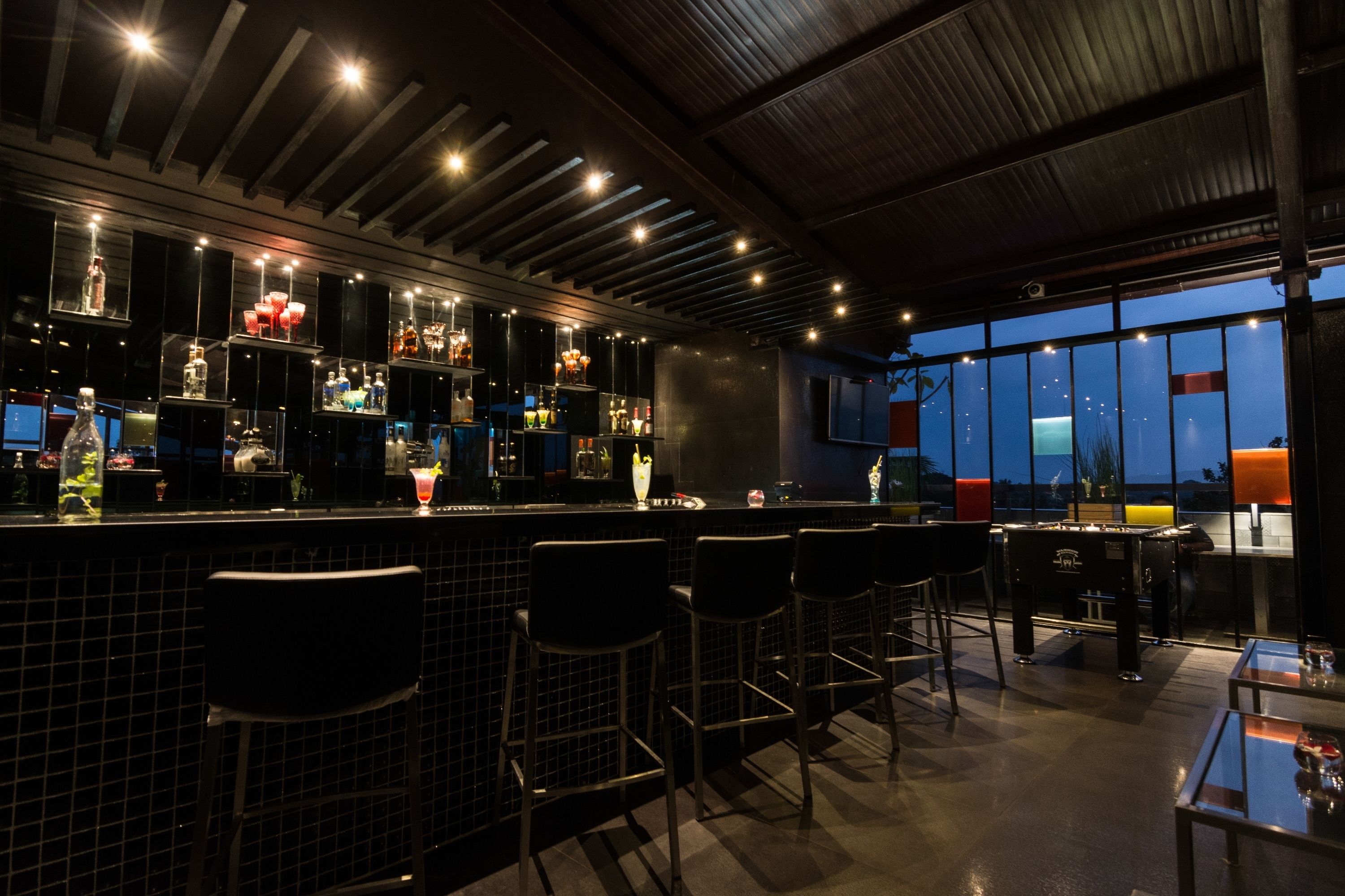 A bar area with a high ceiling, bar stools, and a view of the night sky through large windows.