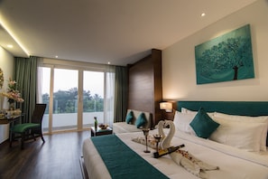 A hotel room with a large bed, two bedside tables, a chair, a painting, and a view of greenery through the window.