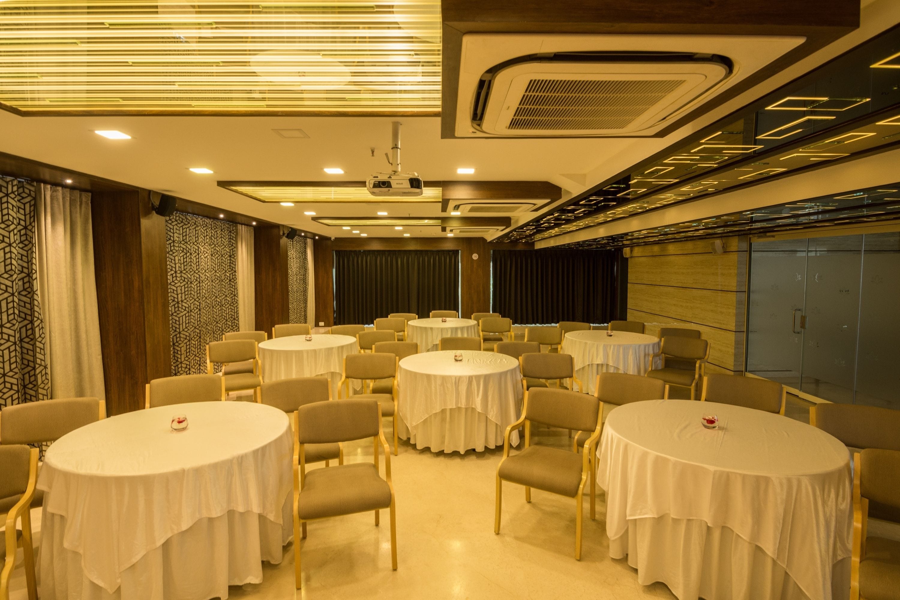 A conference room with multiple round tables, each covered with a white tablecloth, and surrounded by chairs.