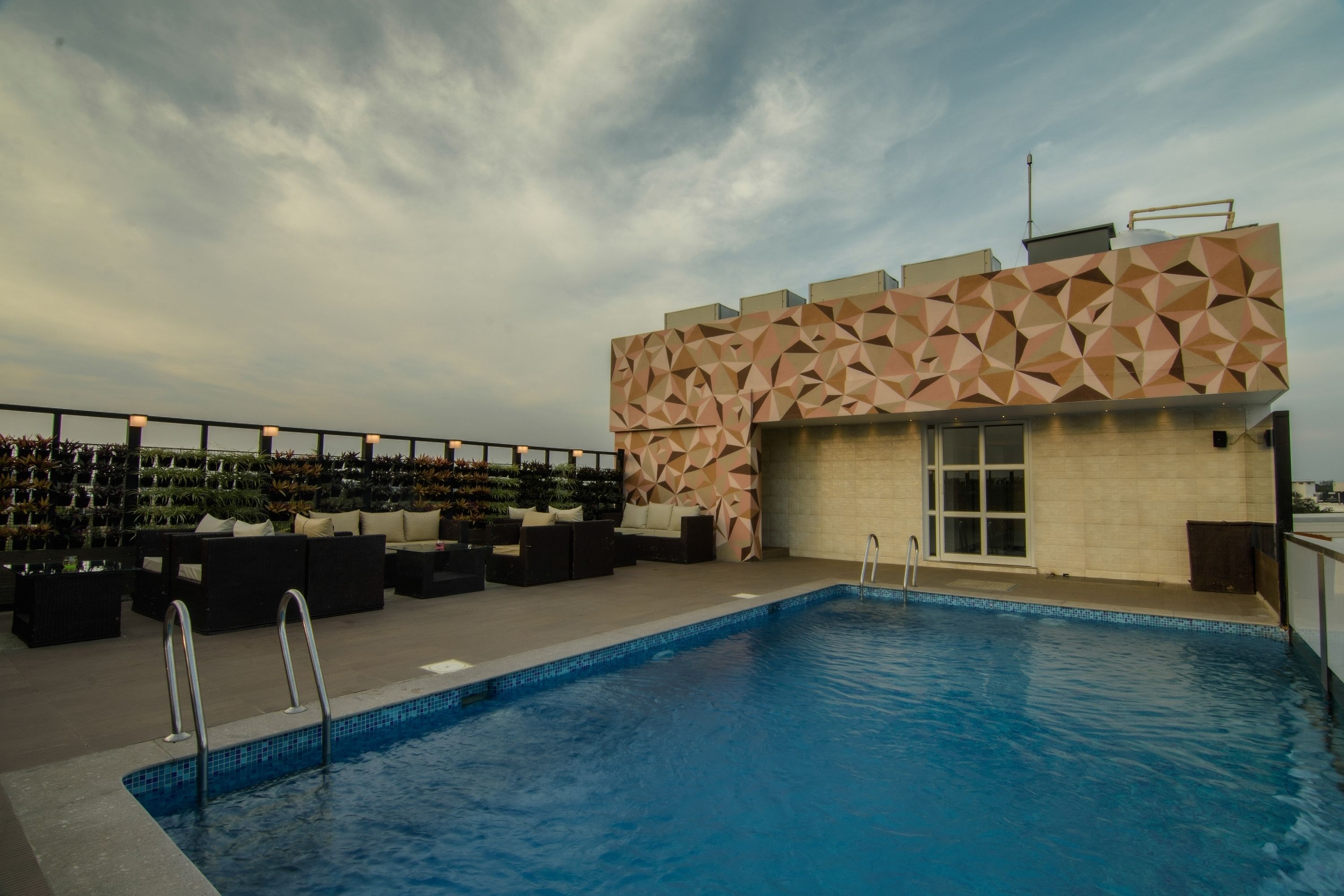 A rooftop pool area with a geometric-patterned wall, outdoor seating, and a clear sky.