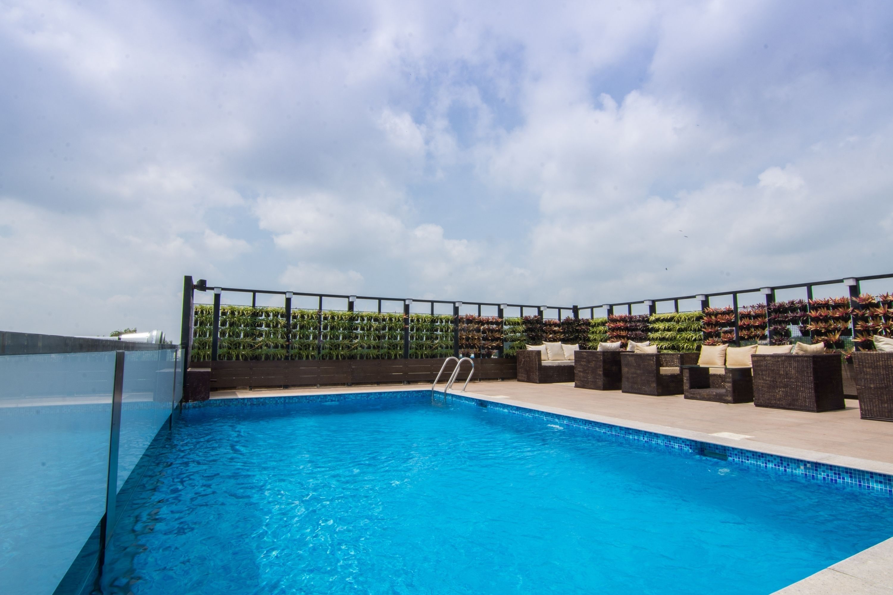 Una piscina en la azotea con vistas despejadas del cielo, rodeada de mobiliario exterior y un muro ajardinado.
