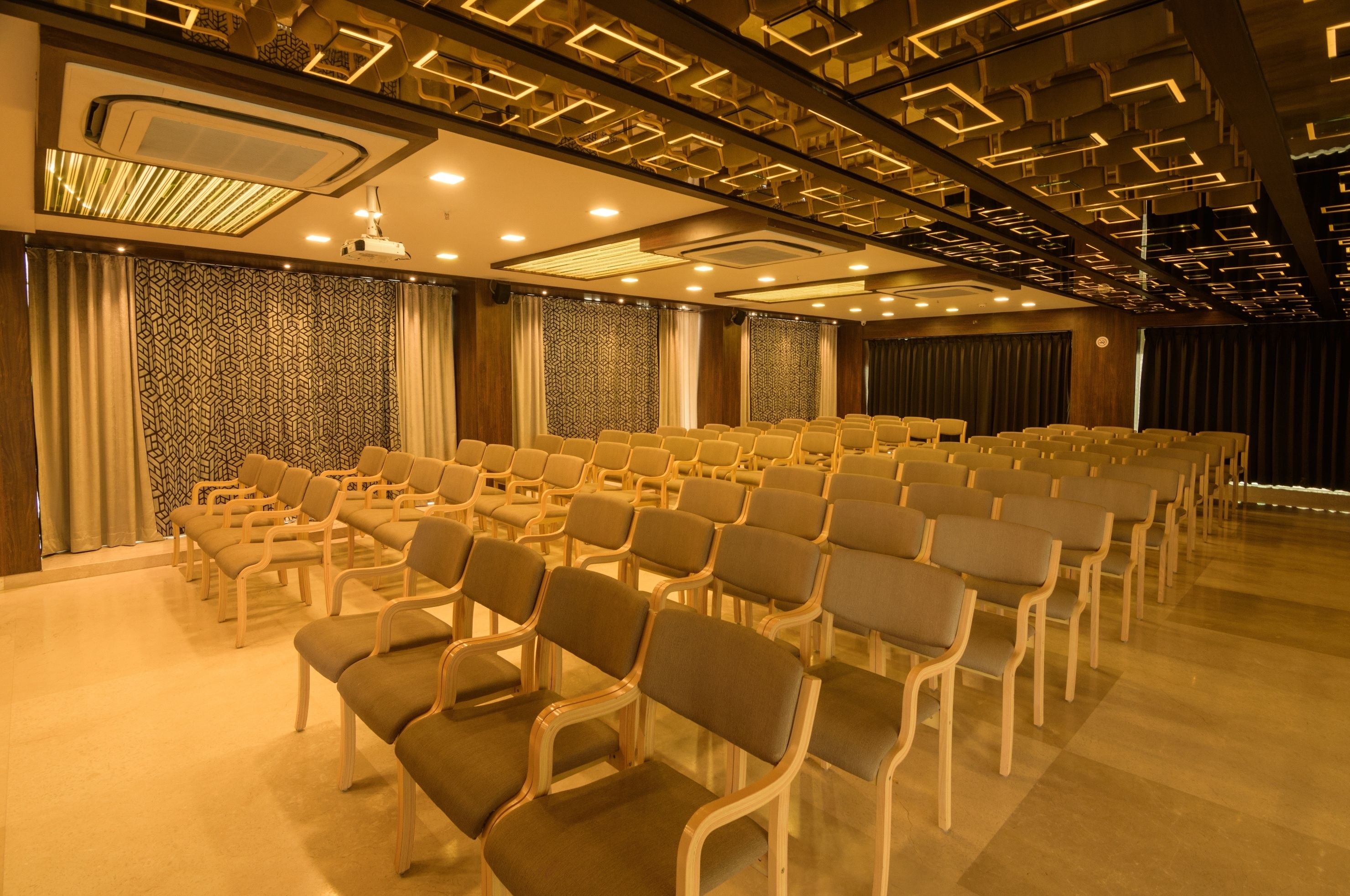 A conference room with rows of chairs, a patterned wall, and a stage with curtains.