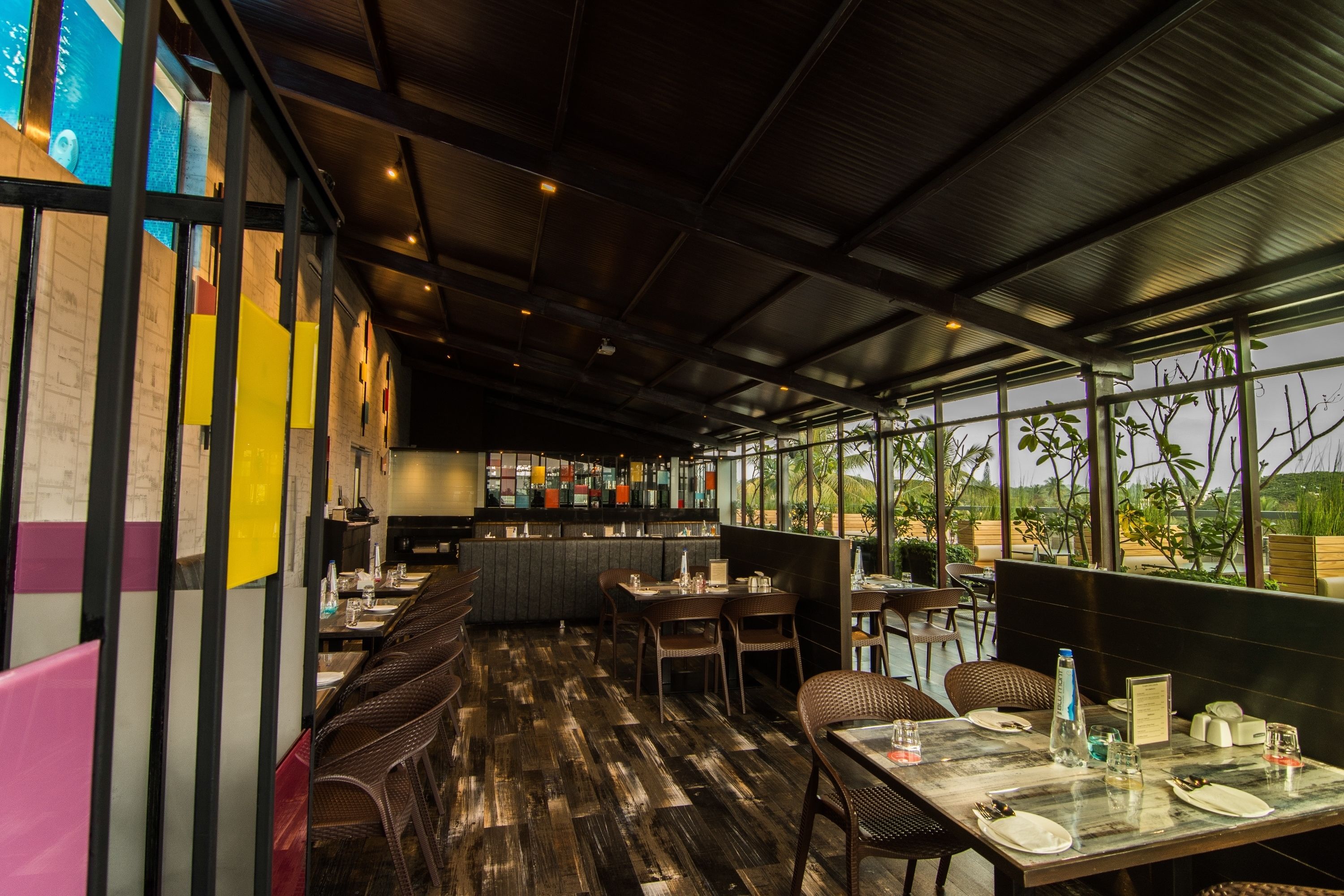 A restaurant with a long counter, high ceiling, and large windows offering a view of the outdoors.