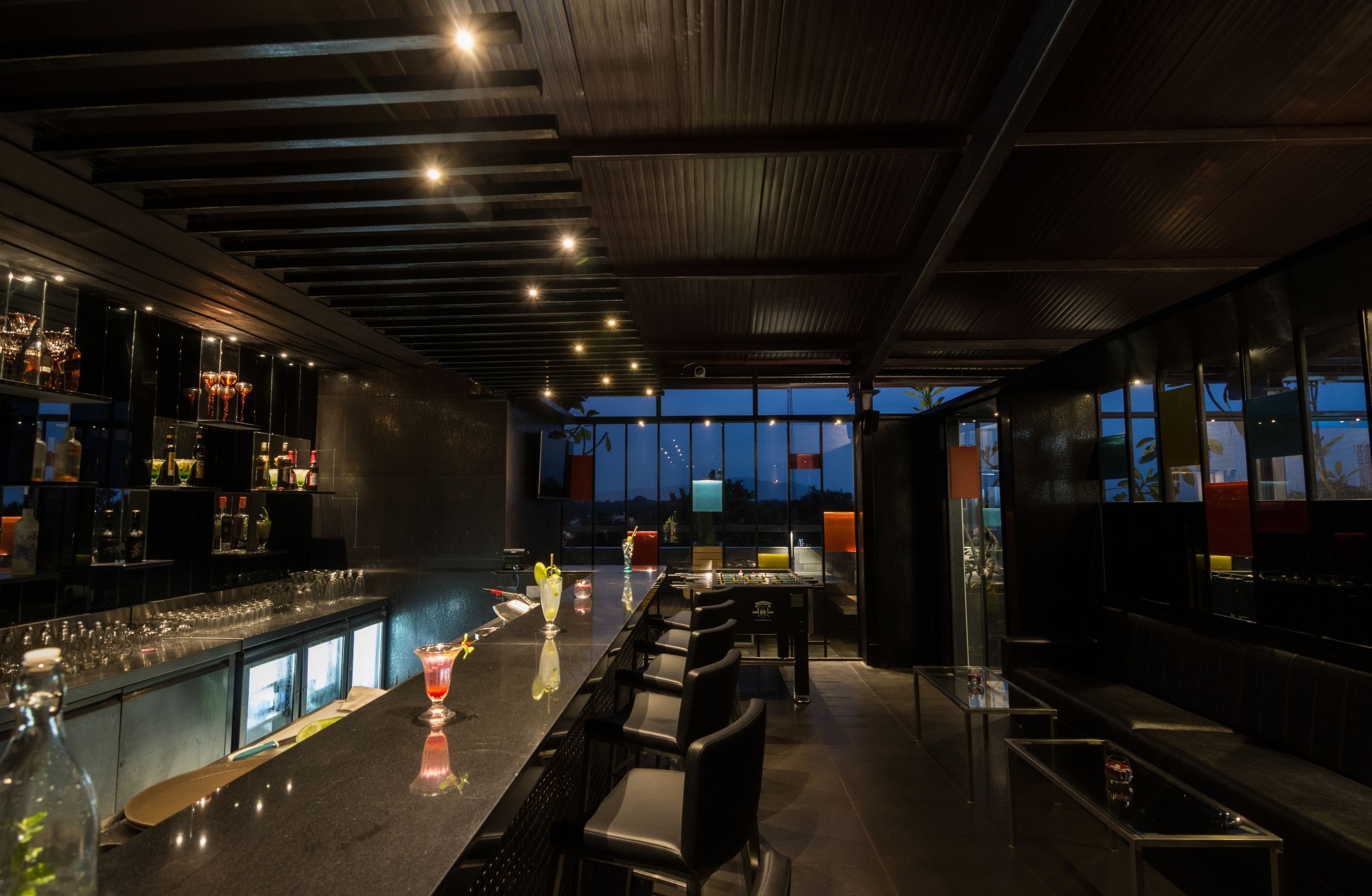 Zona de bar con una barra larga, diversas opciones de asientos y vistas al exterior a través de amplios ventanales.