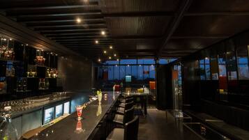 Zona de bar con una barra larga, diversas opciones de asientos y vistas al exterior a través de amplios ventanales.
