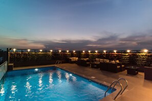 A rooftop pool area with a clear blue pool, surrounded by lounge chairs and a row of lights.