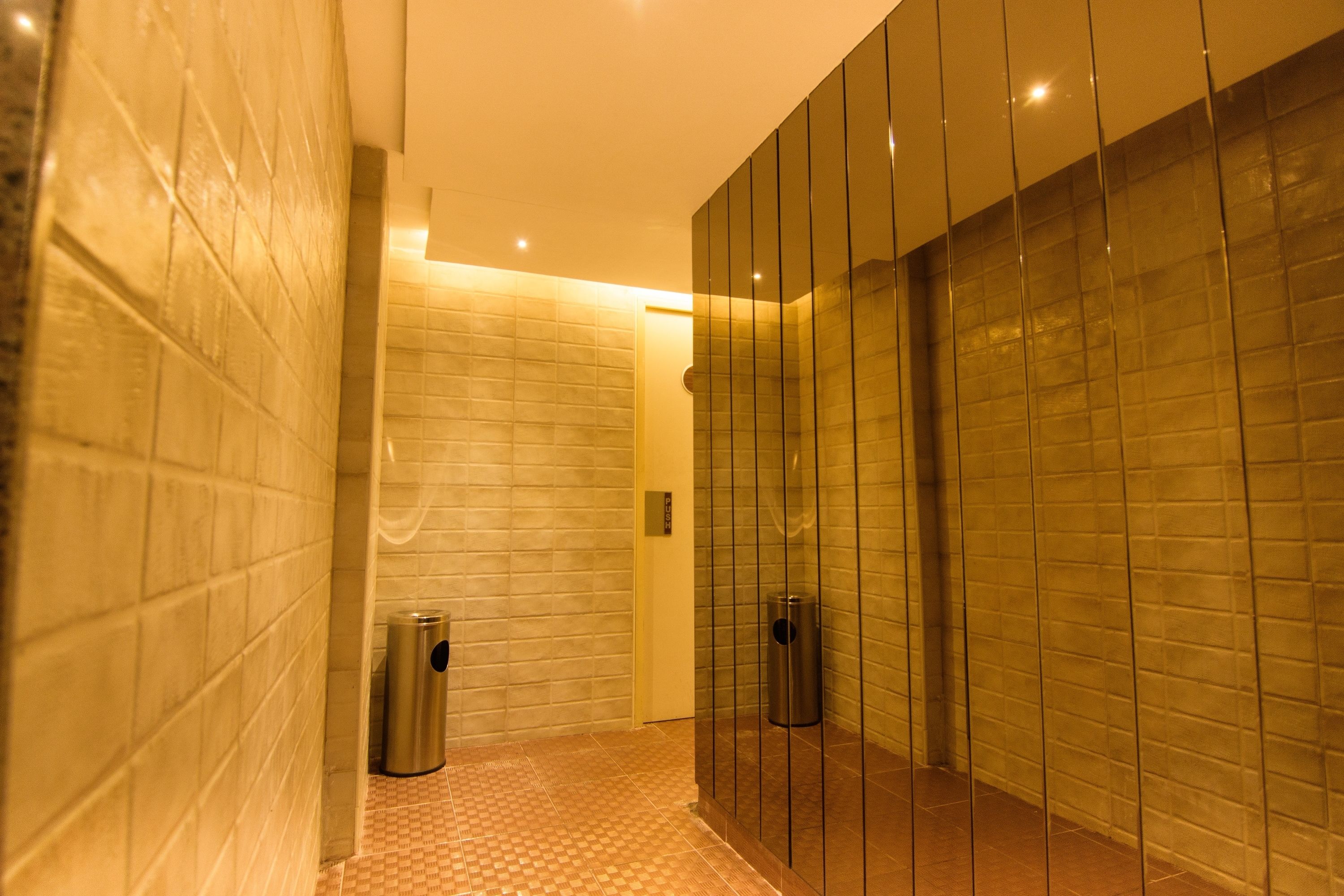 A modern bathroom with tiled walls, a glass partition, and a trash bin.