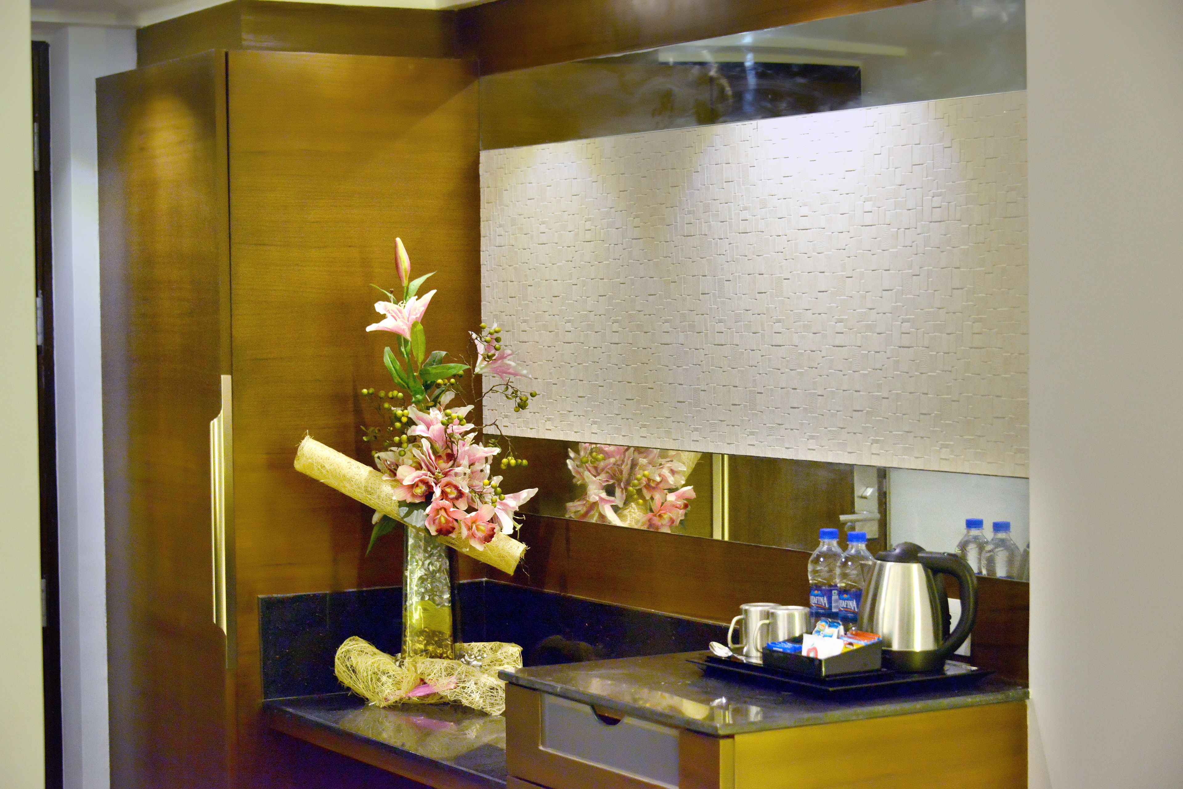A hotel room with a wooden cabinet, a vase with flowers, a mirror, and a coffee maker on the counter.
