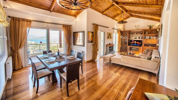 A spacious living area with a wooden ceiling, a dining table set for four, a sofa, and a bookshelf. - Glan Y Mor (Agios Nikolaos)