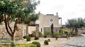 A stone building with a circular window and a stone pathway leading to a seating area. - Glan Y Mor (Agios Nikolaos)