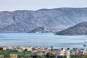 A coastal town with buildings along the waterfront, a clear view of the sea, and a hilly backdrop.