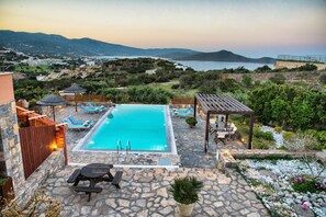 A pool area with lounge chairs, a pergola, and a stone patio.