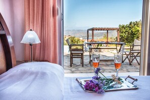 A hotel room with a bed, a table with a tray of flowers and two glasses of wine, and a view of an outdoor patio with a table and chairs.
